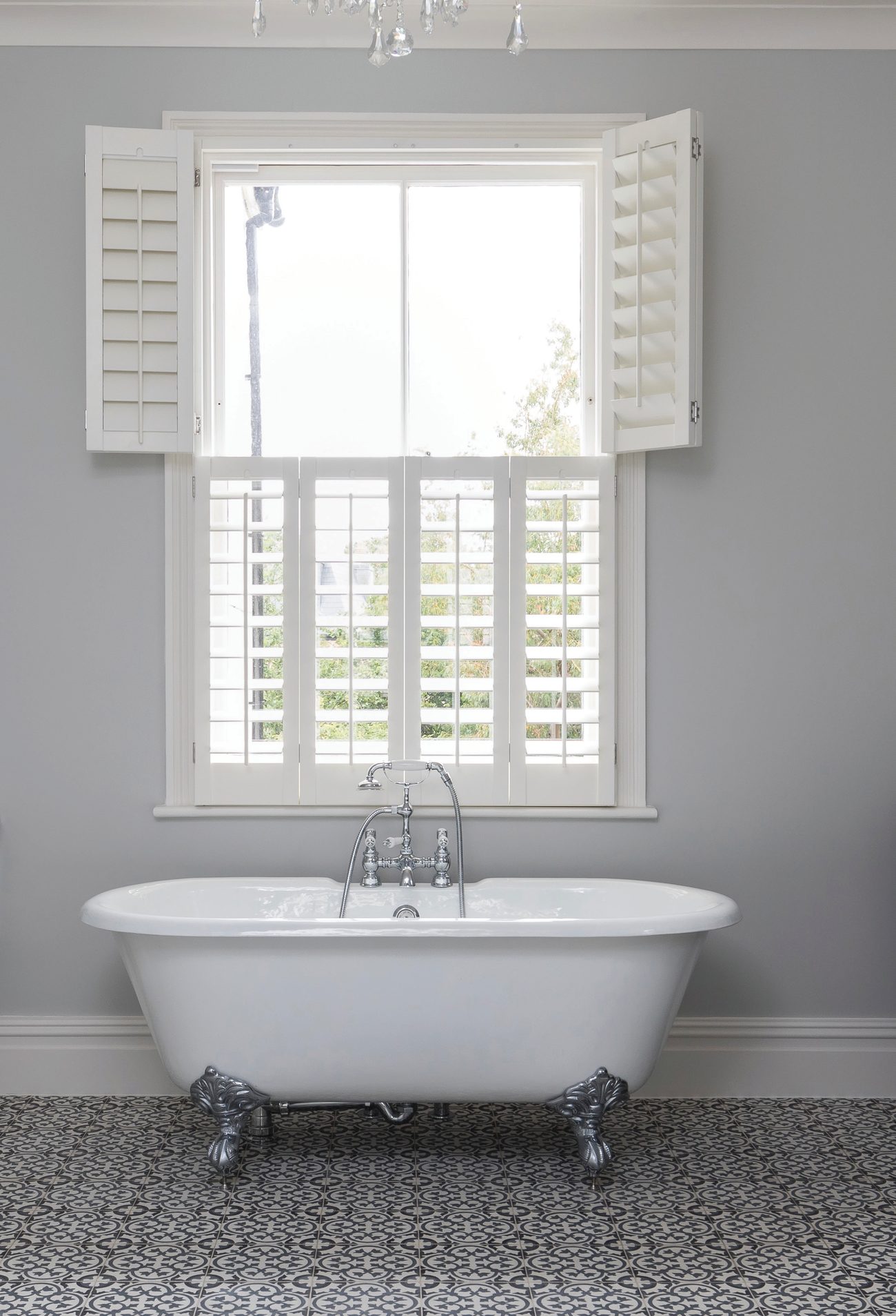 Tier on tier white shutters above a freestanding clawfoot bath